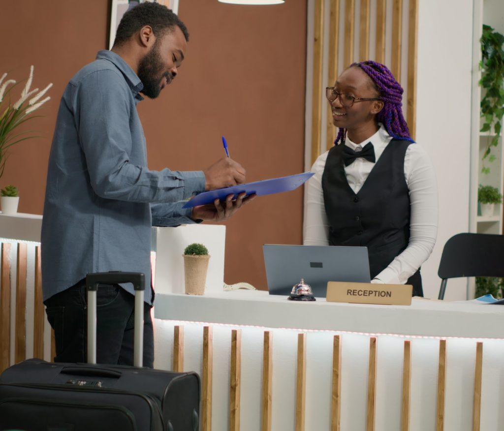 Guest filling in registration forms and signing papers before seeing room, finishing with check in. Employee providing luxurious concierge services, greeting people at front desk. Handheld shot.